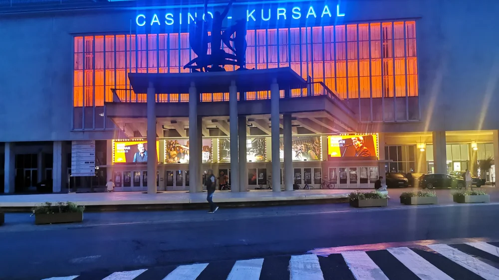 Het Kursaal Oostende bij avond, met een verlichte glazen gevel onder een blauwe lucht.