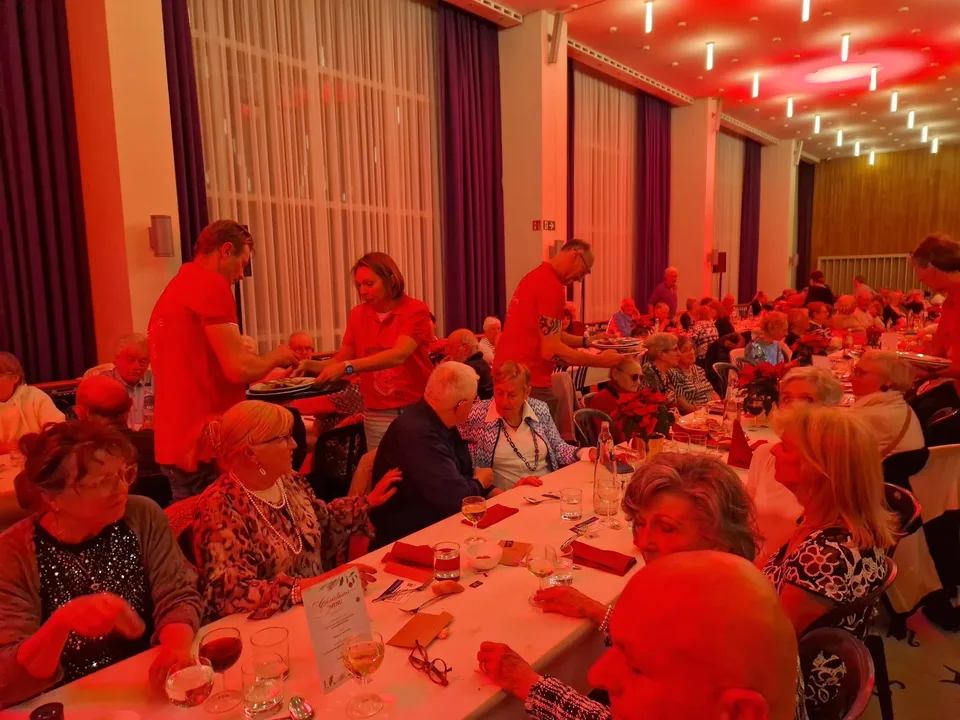 Vrijwilligers bedienen gasten aan de lange gedekte tafels tijdens het kerstfeest van 2025.